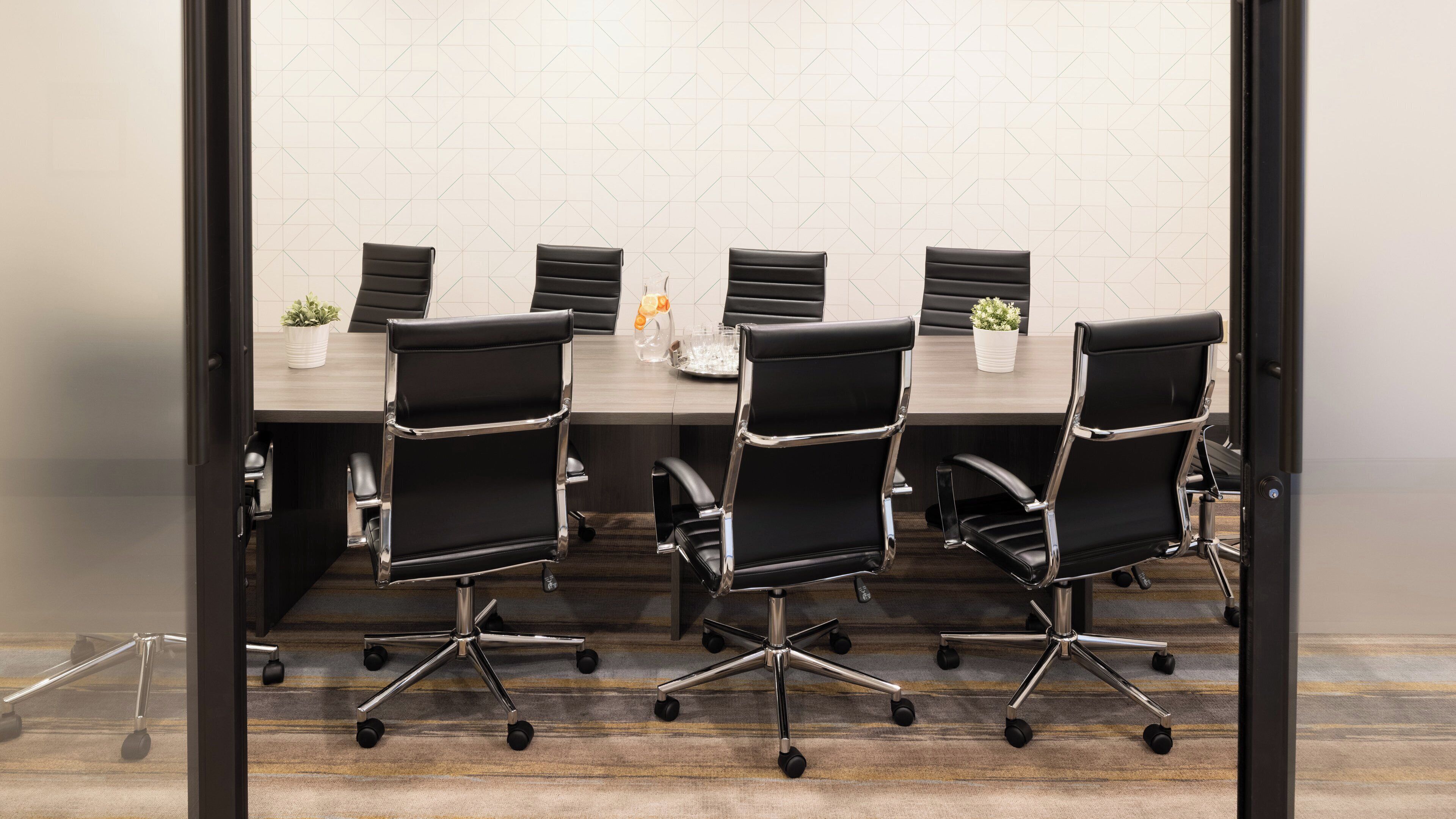 A conference room with a long table and four black office chairs with chrome accents.
