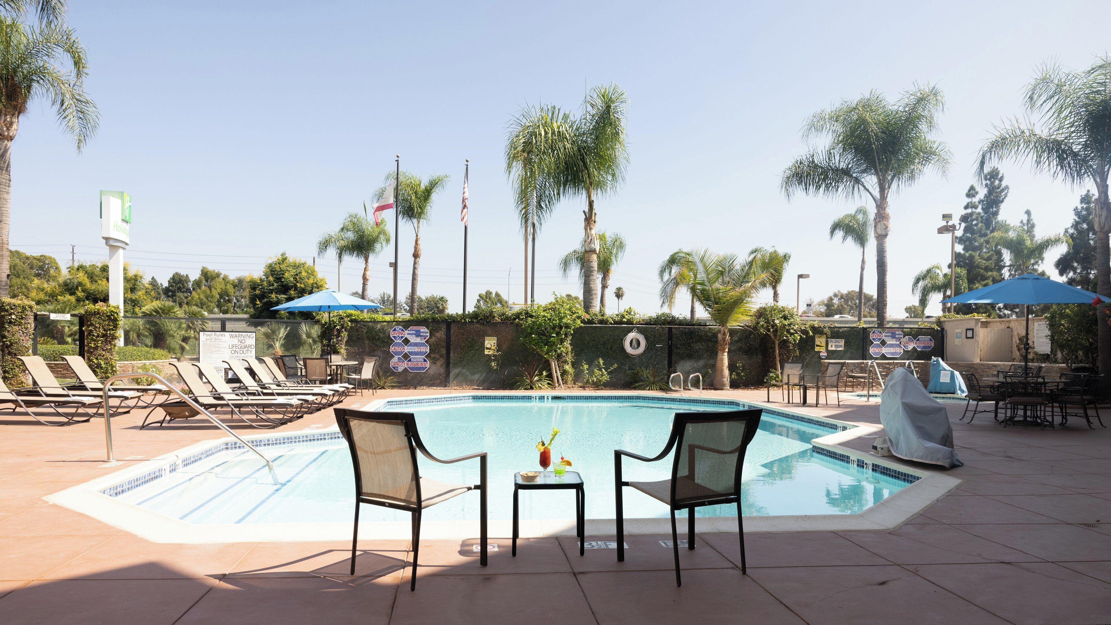 A pool area with lounge chairs, umbrellas, and a small table with a drink.