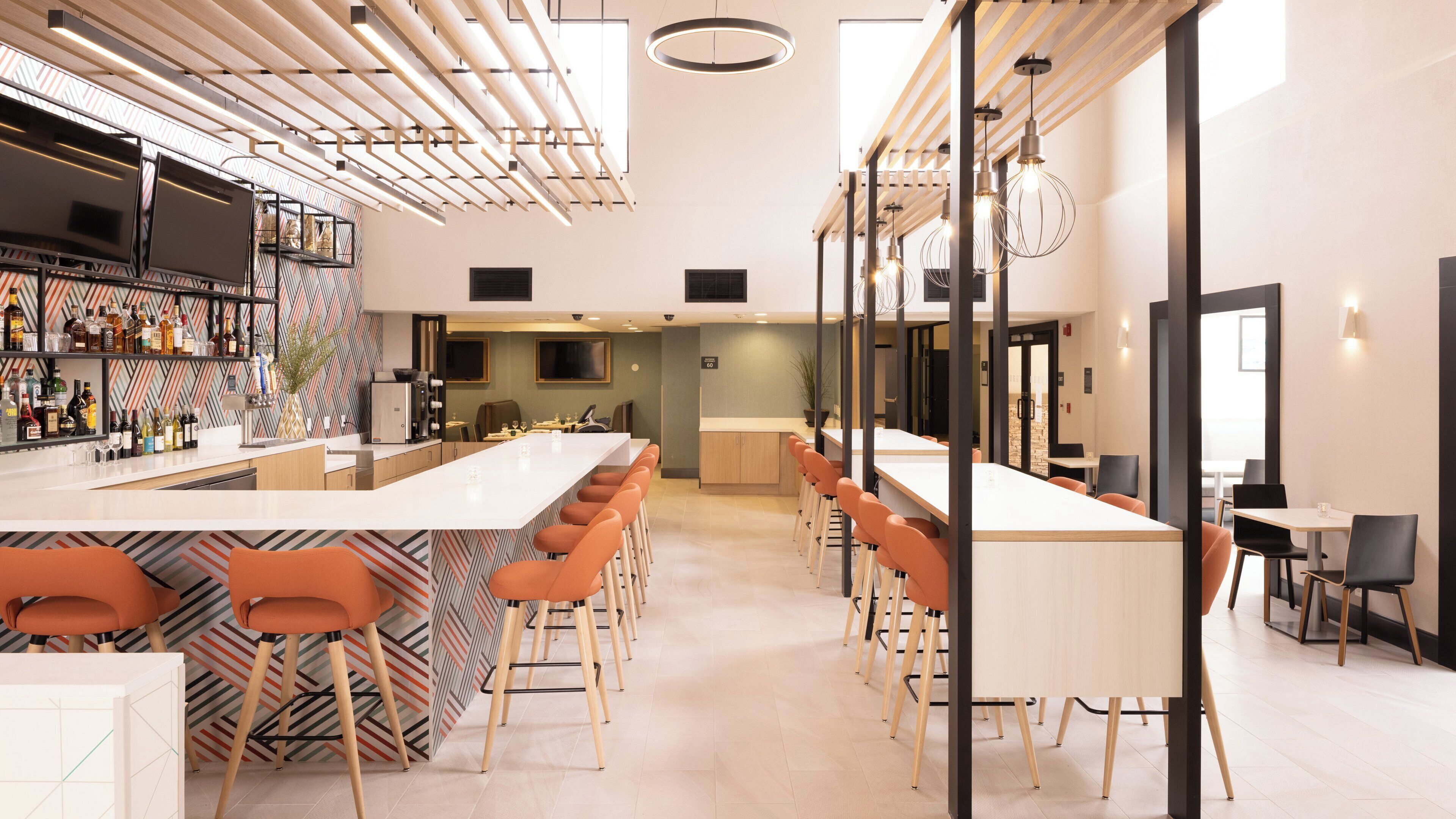 A modern bar area with a long counter, multiple bar stools, and a variety of bottles on shelves.