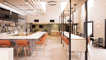A modern bar area with a long counter, multiple bar stools, and a variety of bottles on shelves.