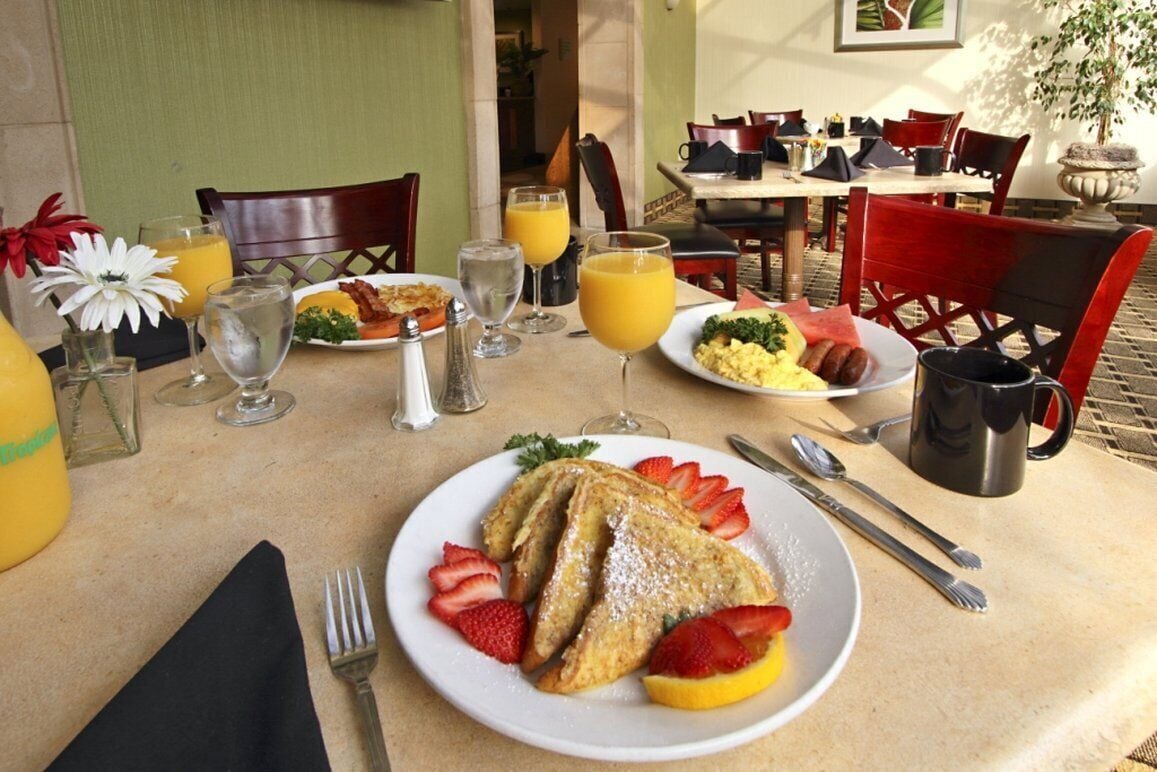 A breakfast setting with a plate of French toast, strawberries, and orange slices, a glass of orange juice, and a coffee mug.