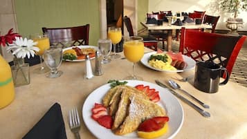 A breakfast setting with a plate of French toast, strawberries, and orange slices, a glass of orange juice, and a coffee mug.