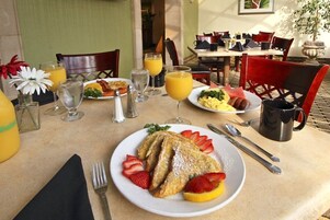 A breakfast setting with a plate of French toast, strawberries, and orange slices, a glass of orange juice, and a coffee mug.