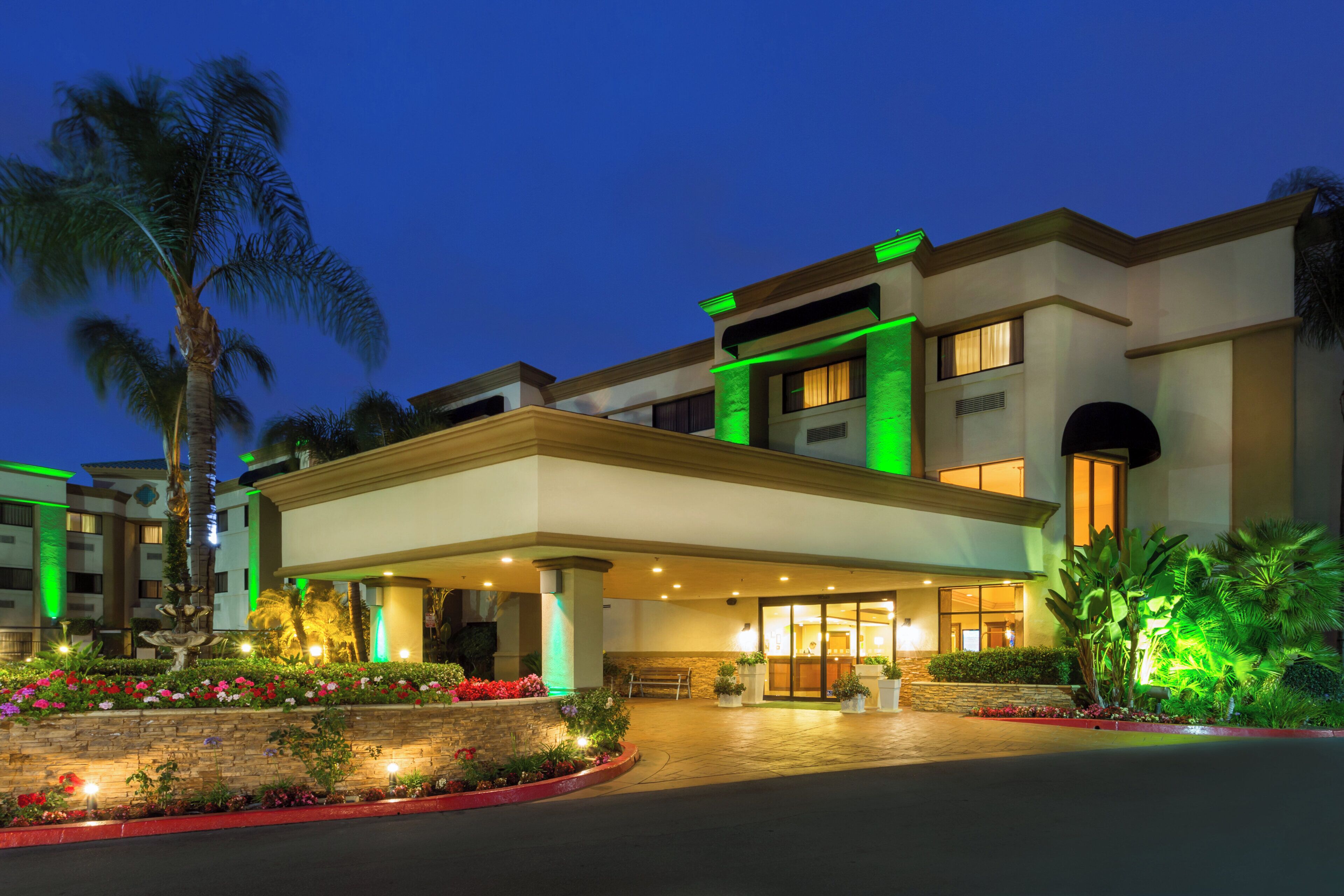 A hotel with a covered entrance, palm trees, and a well-lit facade.