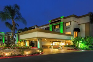 Un hotel con entrada cubierta, palmeras y una fachada bien iluminada.