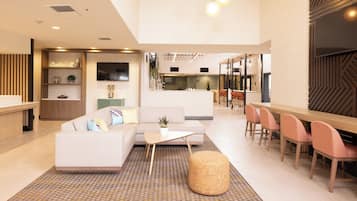 A modern hotel lobby with a reception desk, seating area, and a dining space.