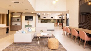 A modern hotel lobby with a reception desk, seating area, and a dining space. - Holiday Inn Santa Ana-Orange Co. Arpt by IHG (Santa Ana)