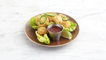 A plate of fried food with jalapeño slices and a small bowl of sauce.
