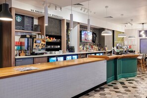 A modern bar area with a coffee machine, shelves with various beverages, and a television screen.