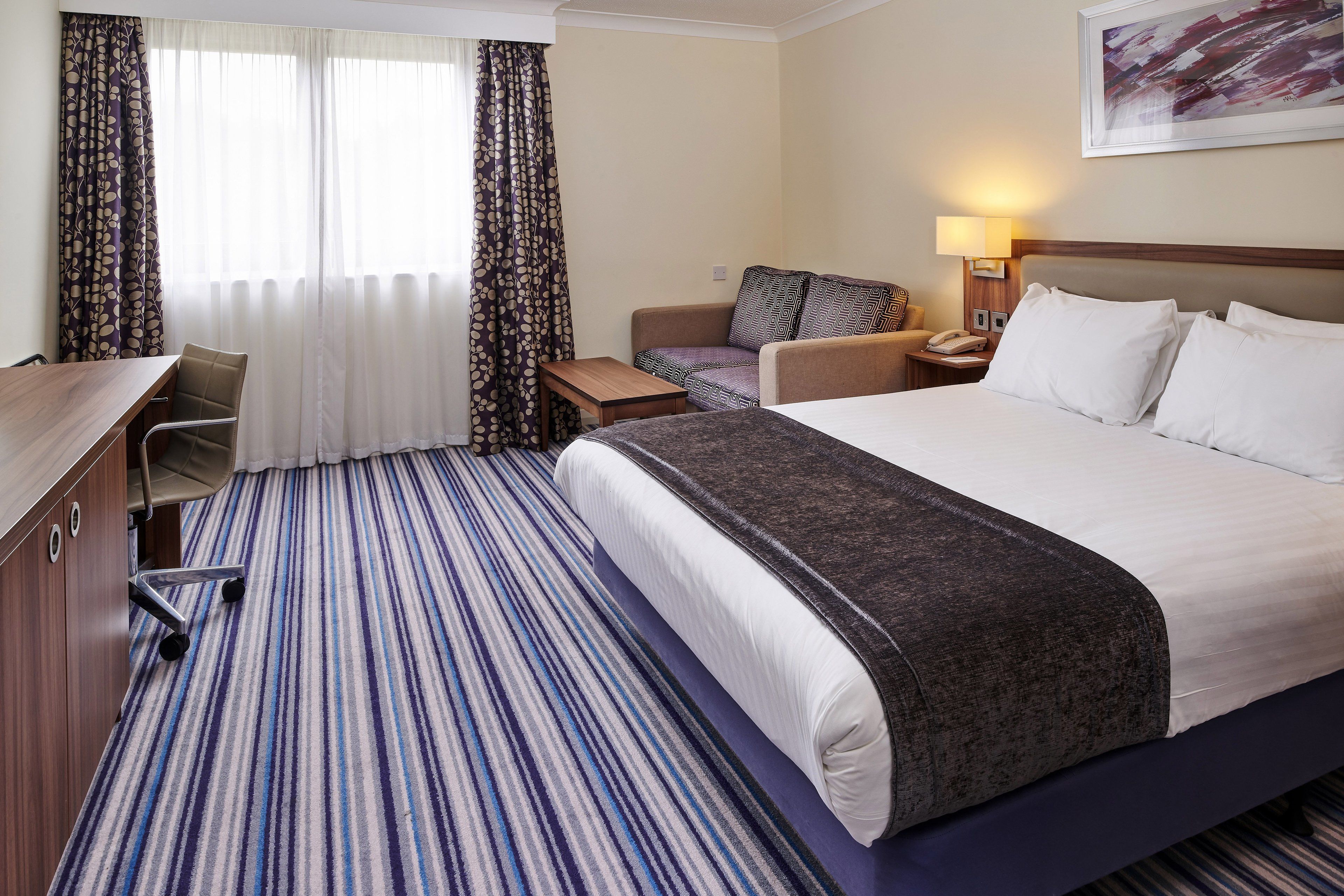A hotel room with a large bed, a desk, a chair, and a sofa.