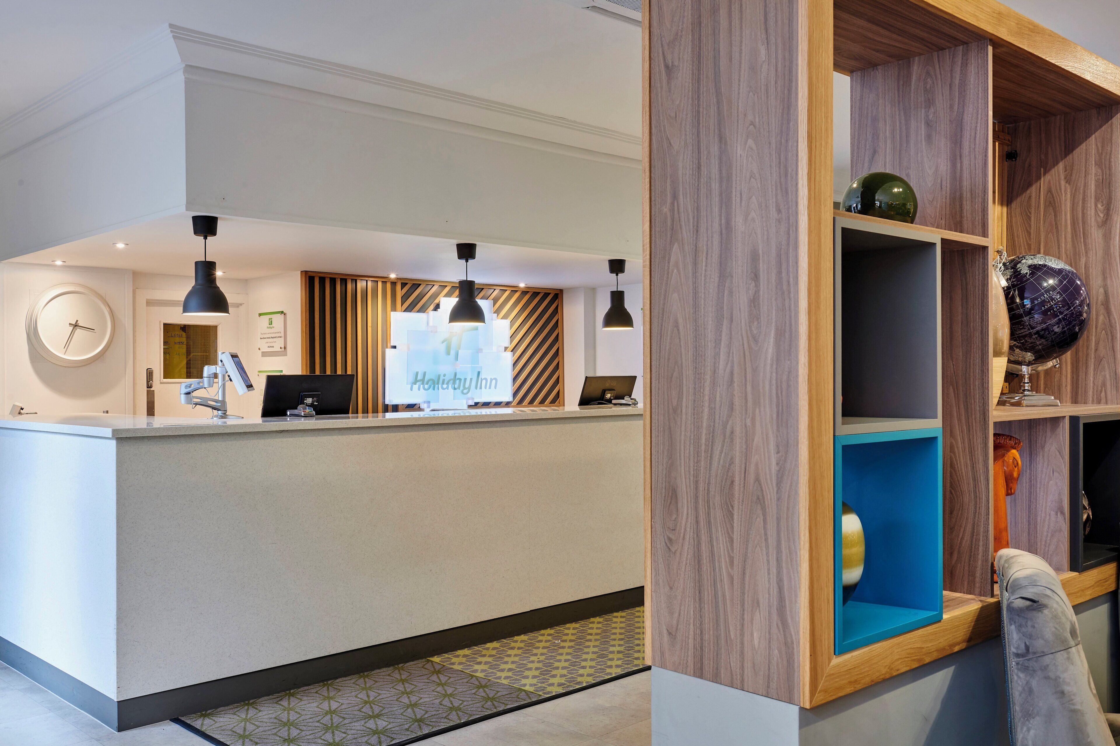 A hotel reception area with a reception desk, a clock, and a sign indicating 'Holiday Inn'.