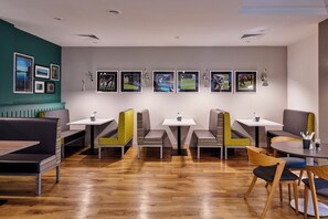 A modern restaurant interior with wooden flooring, multiple seating options including booths and tables, and a wall adorned with framed photographs. - Holiday Inn Haydock M6 Jct23 by IHG (Newton-le-Willows)