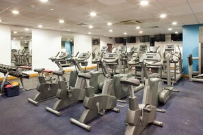 A gym with multiple stationary bikes and cardio machines, a mirror wall, and a blue accent wall.