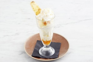 A dessert in a clear glass on a brown plate with a napkin underneath.