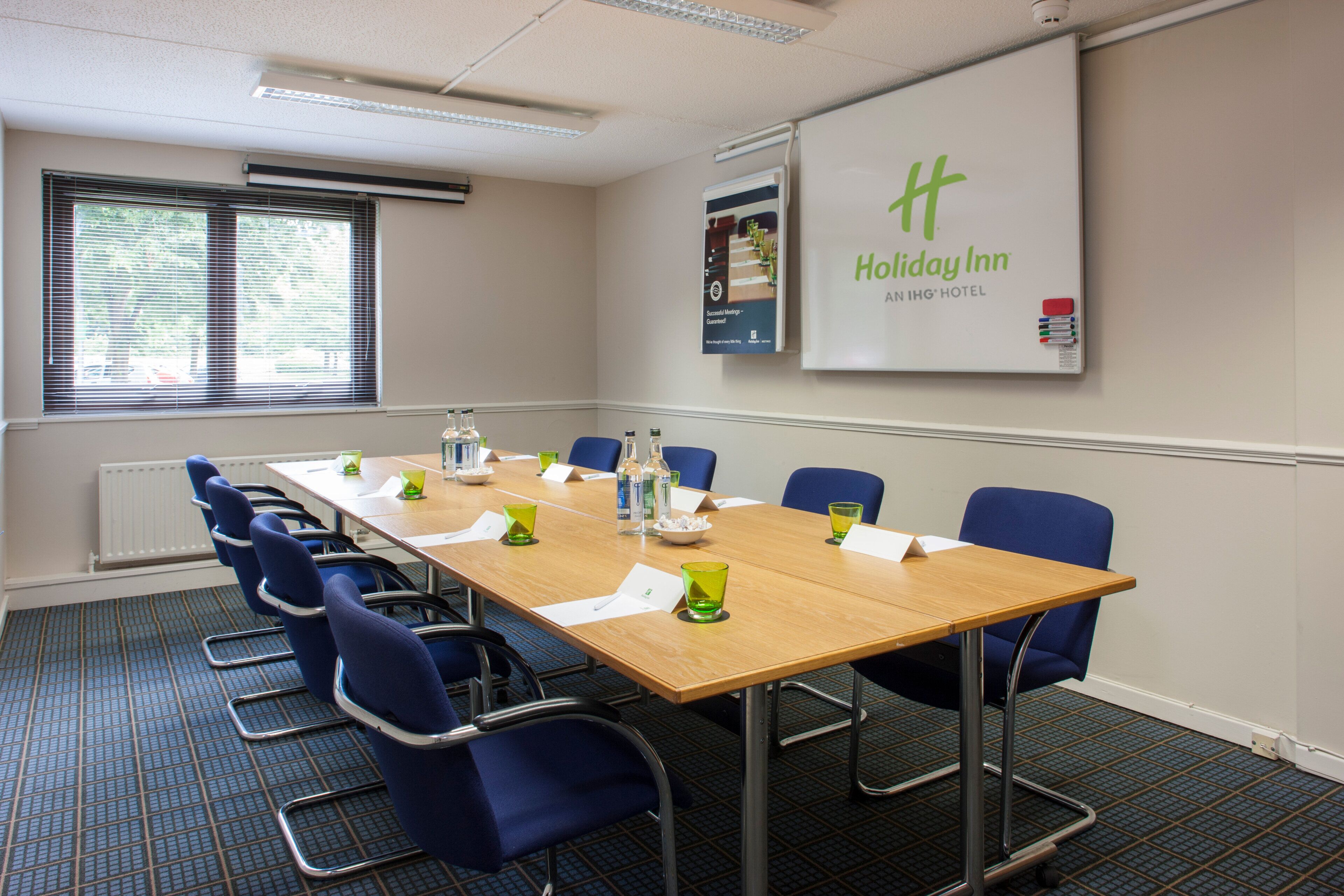 A conference room with a long table, blue chairs, and a Holiday Inn sign on the wall.