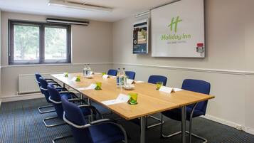 A conference room with a long table, blue chairs, and a Holiday Inn sign on the wall.