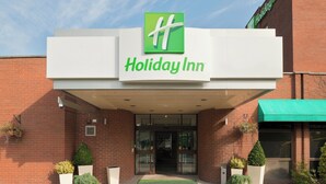 A Holiday Inn hotel entrance with a clear sky, brick facade, and potted plants.