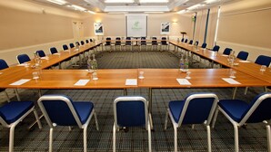A conference room with a long table, blue chairs, and a projector screen.