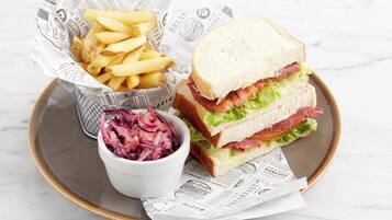Una bandeja con un sándwich, papas fritas y ensalada de col sobre una superficie de mármol.