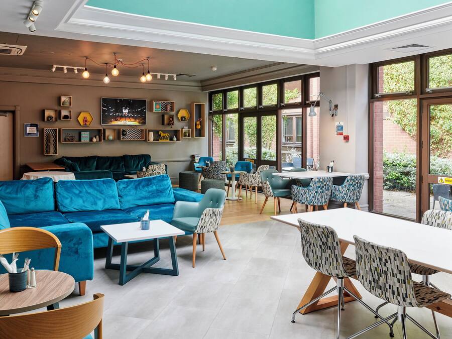 A modern interior with a blue sofa, dining area, and large windows.