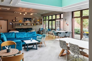 A modern interior with a blue sofa, dining area, and large windows.