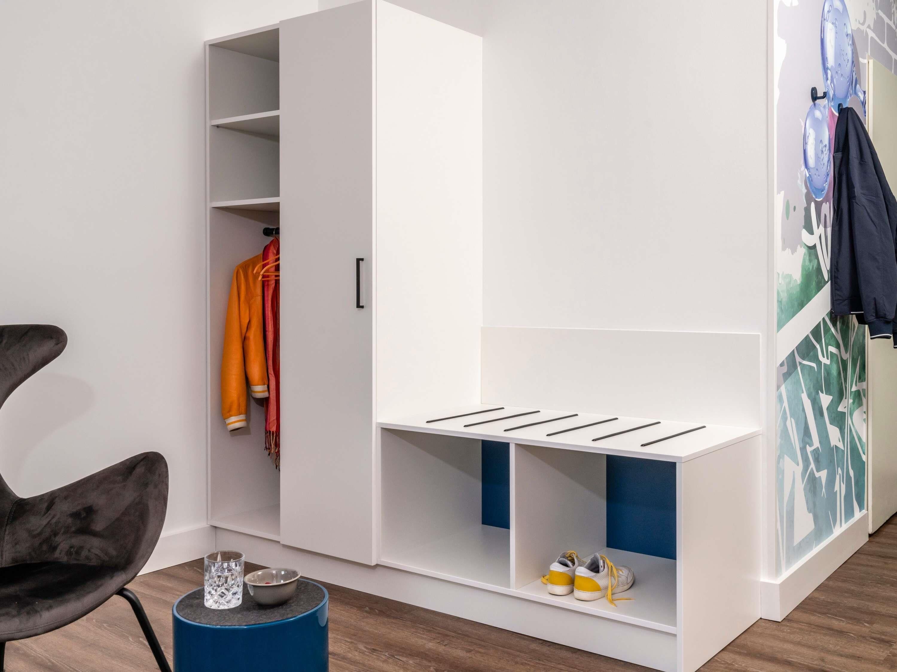 Ein Zimmer mit einem weißen Kleiderschrank, einem blauen Beistelltisch und einem Stuhl.
