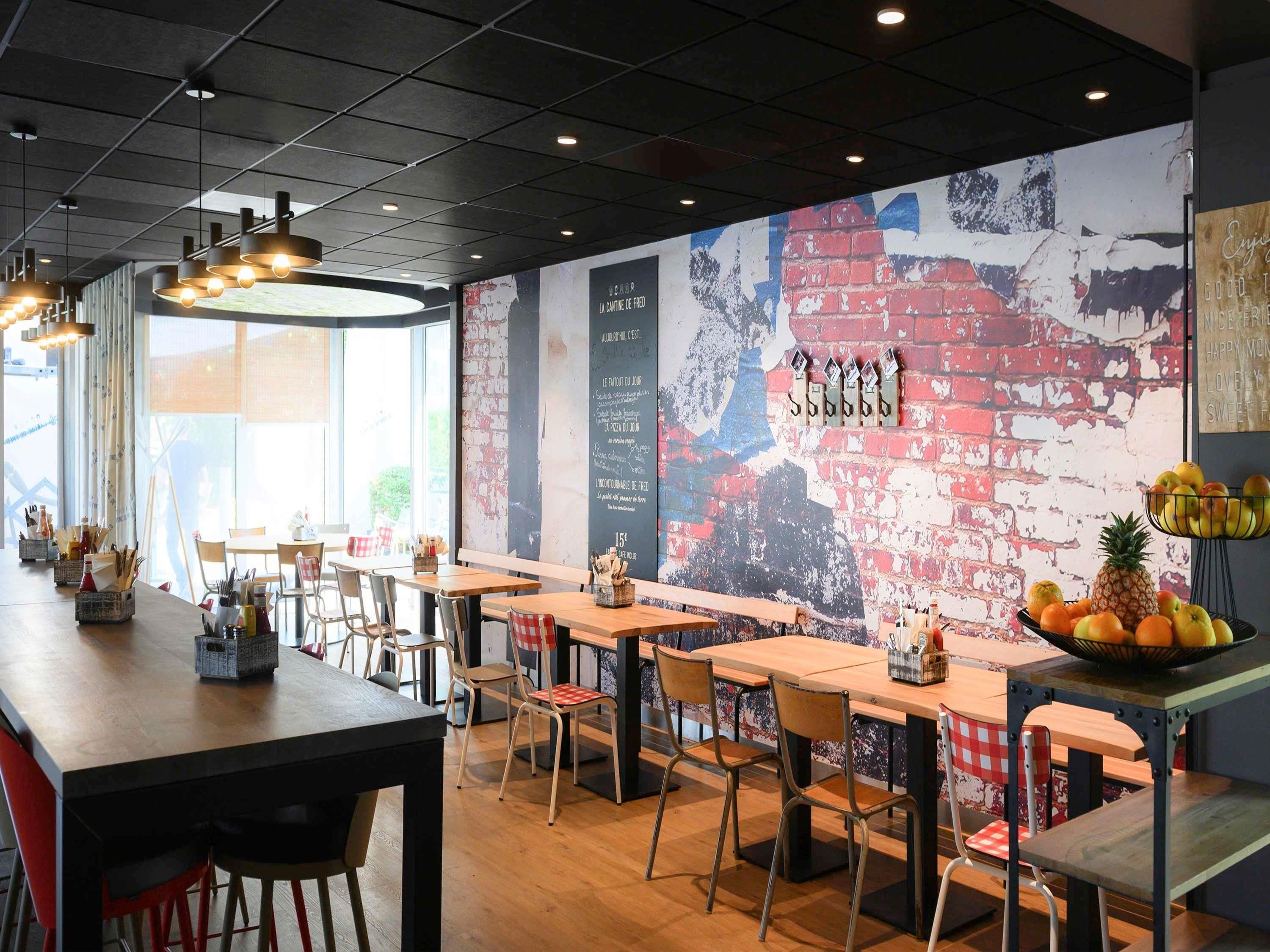 A restaurant interior with wooden tables and chairs, a brick wall mural, and pendant lighting.