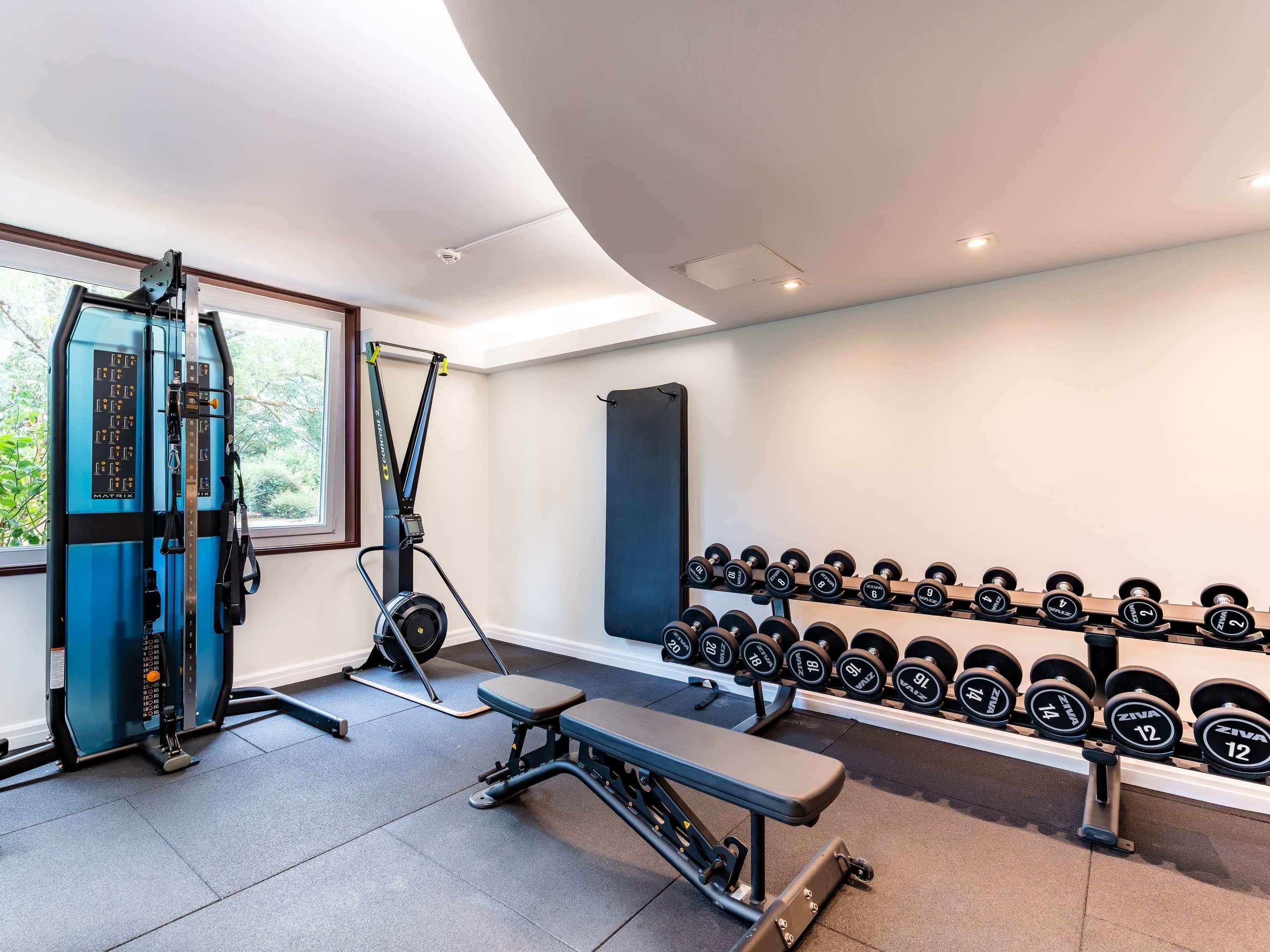 A gym with exercise equipment, a bench, and a rack of dumbbells.