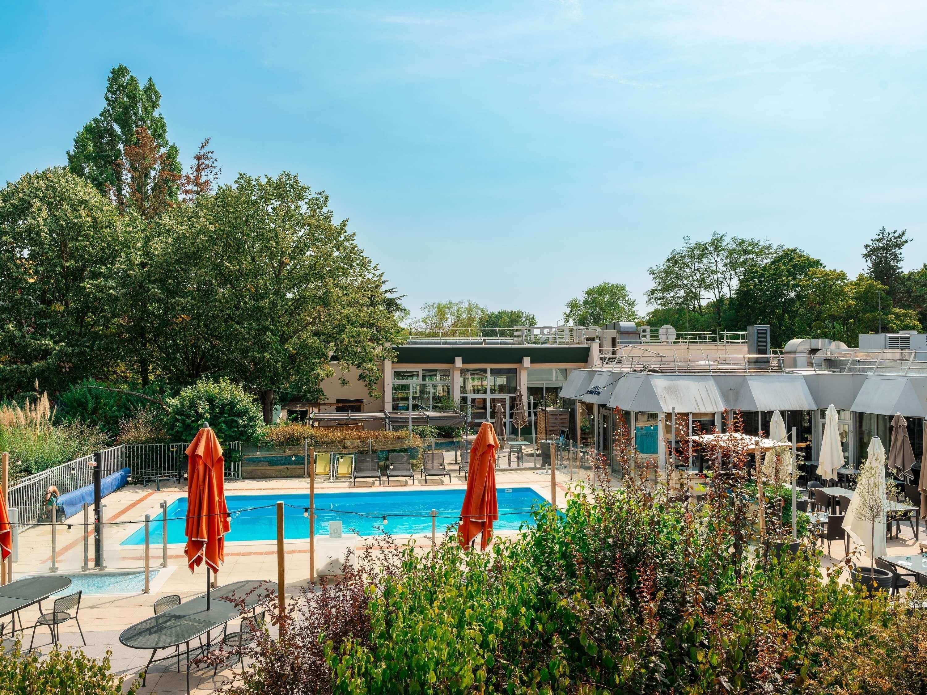 Ein Poolbereich mit Liegestühlen und Sonnenschirmen, umgeben von Pflanzen und einem Gebäude im modernen Stil.