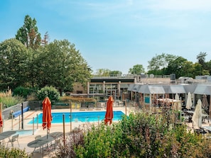 Un área de piscina con sillones de descanso y sombrillas, rodeada de follaje y un edificio de diseño moderno.