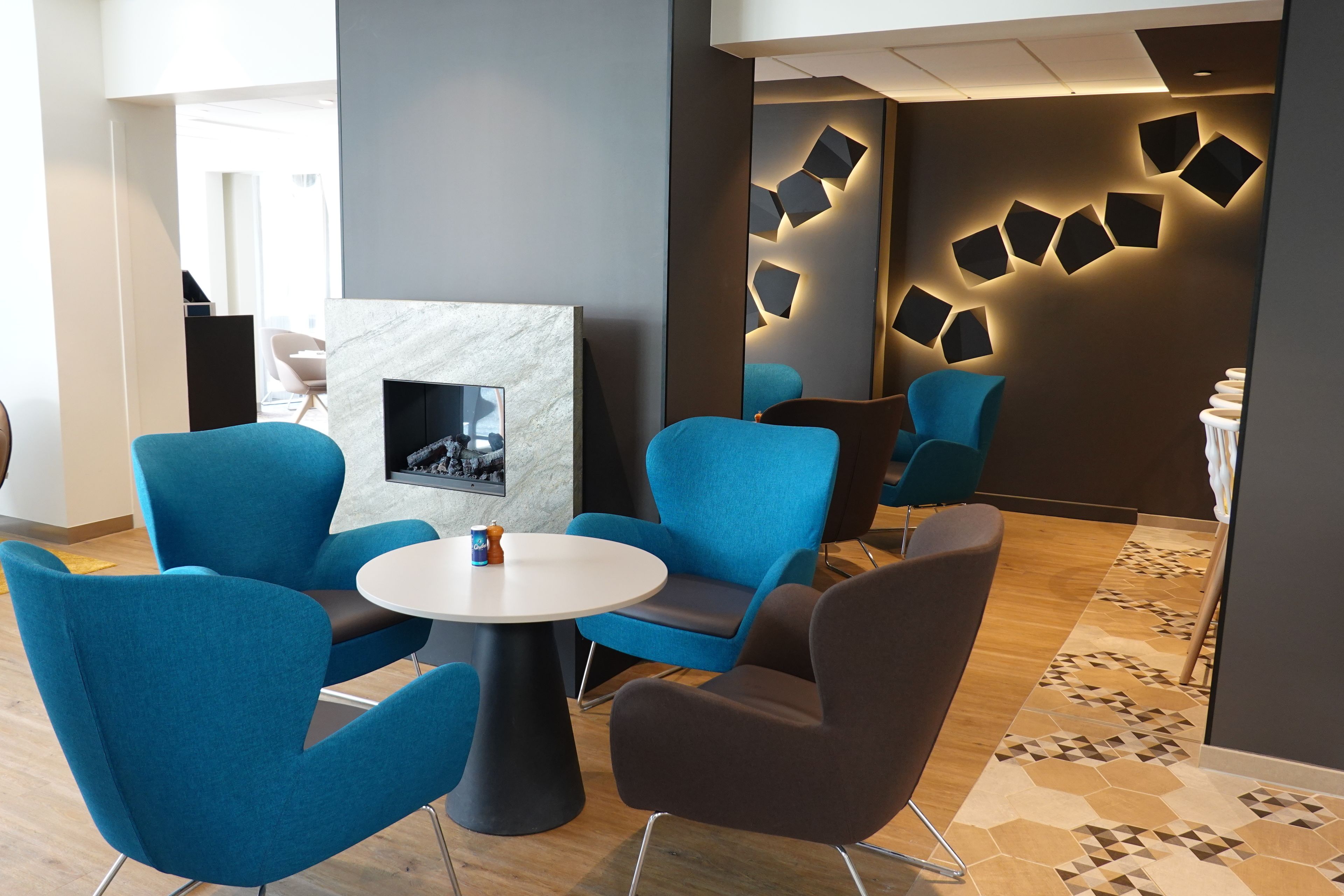 A modern lounge area with blue and brown chairs, a round table, and a marble fireplace.