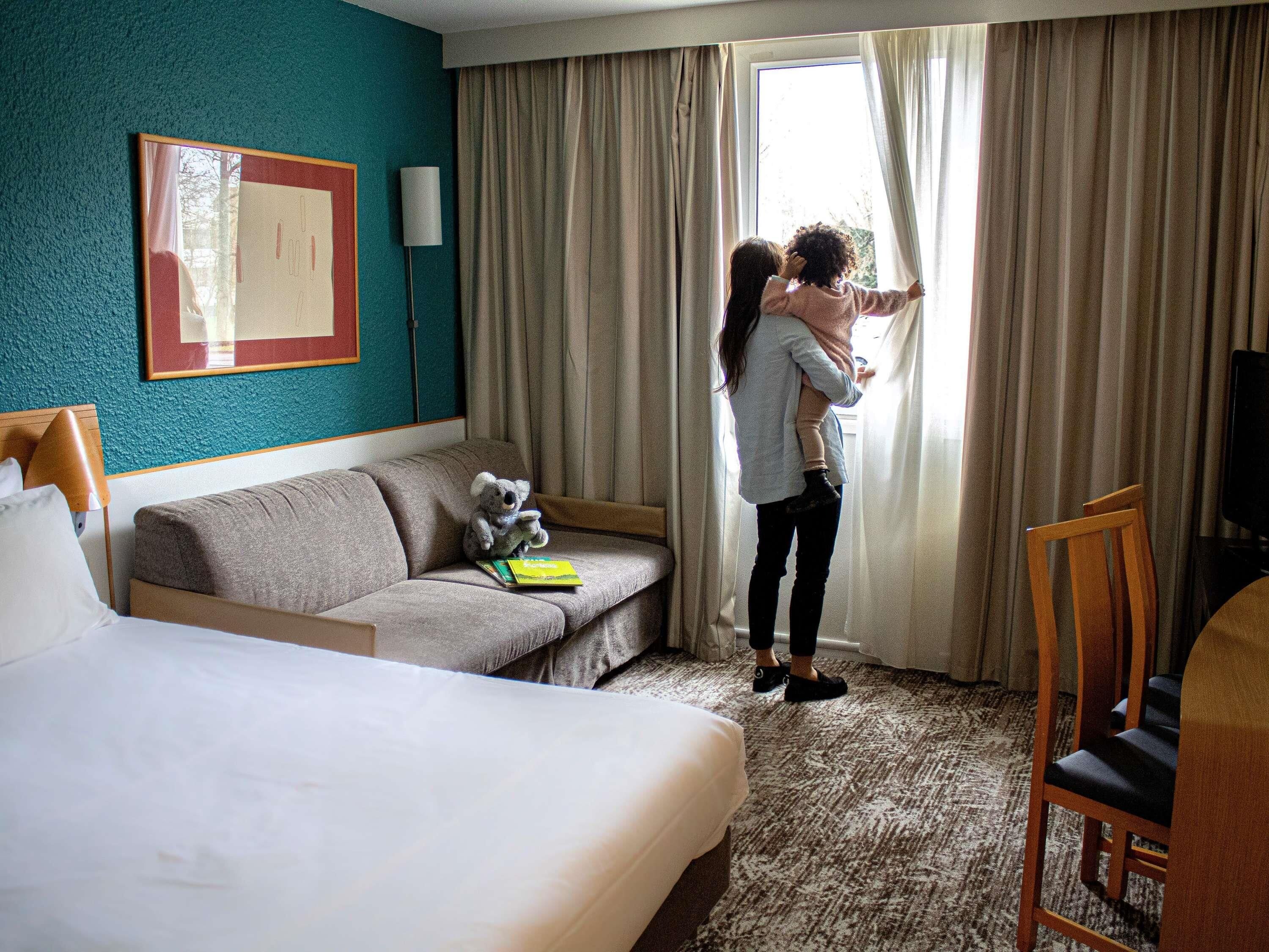 A hotel room with a bed, a sofa, a television, and a window with curtains.