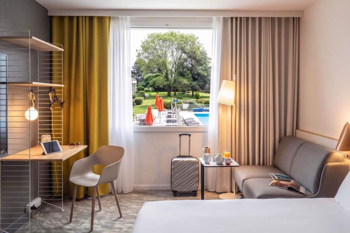 Ein Hotelzimmer mit Bett, Schreibtisch, Stuhl und Blick auf einen Pool und Grünflächen.