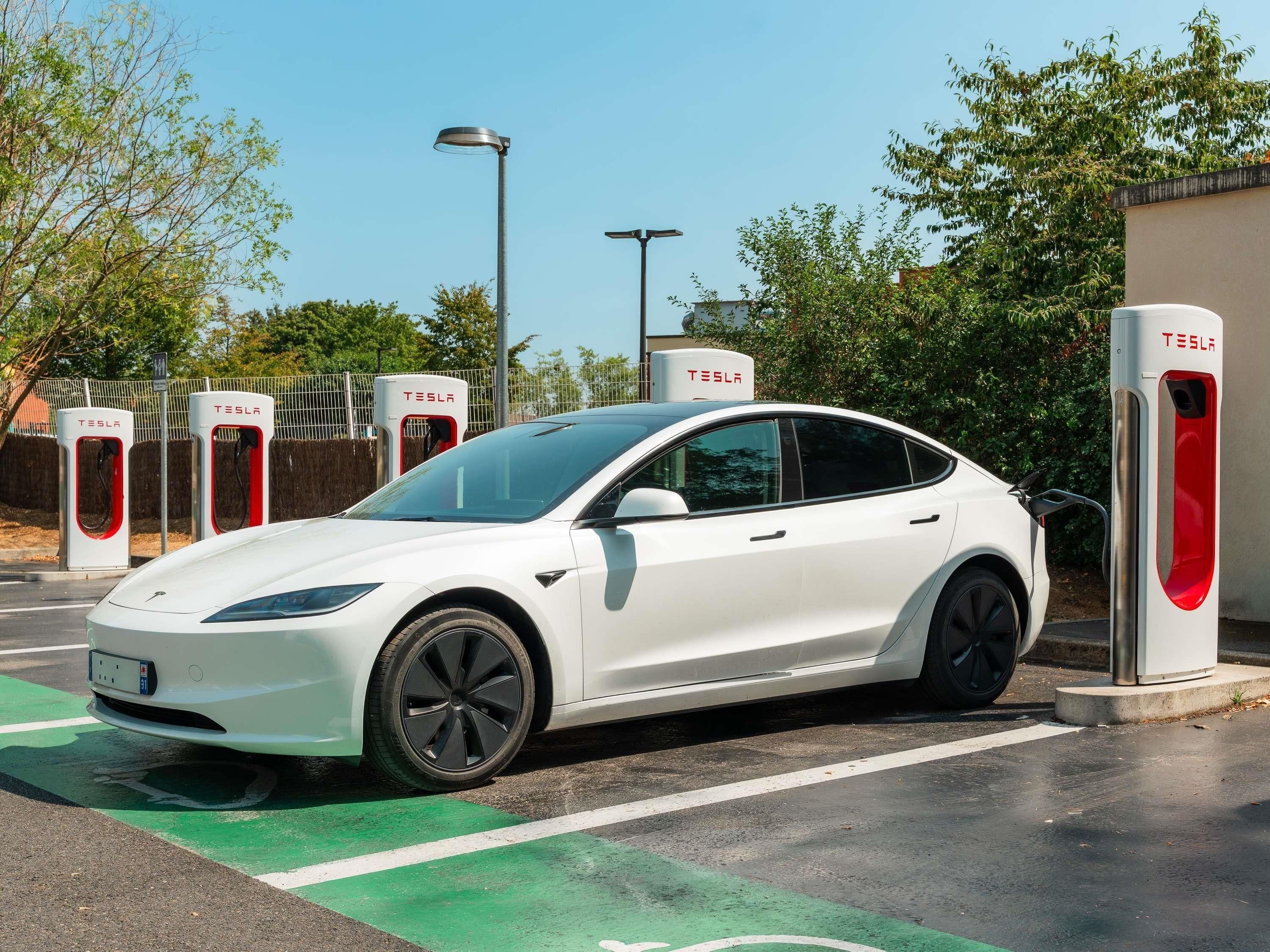 Un Tesla blanco cargando en una estación con un espacio de estacionamiento verde.
