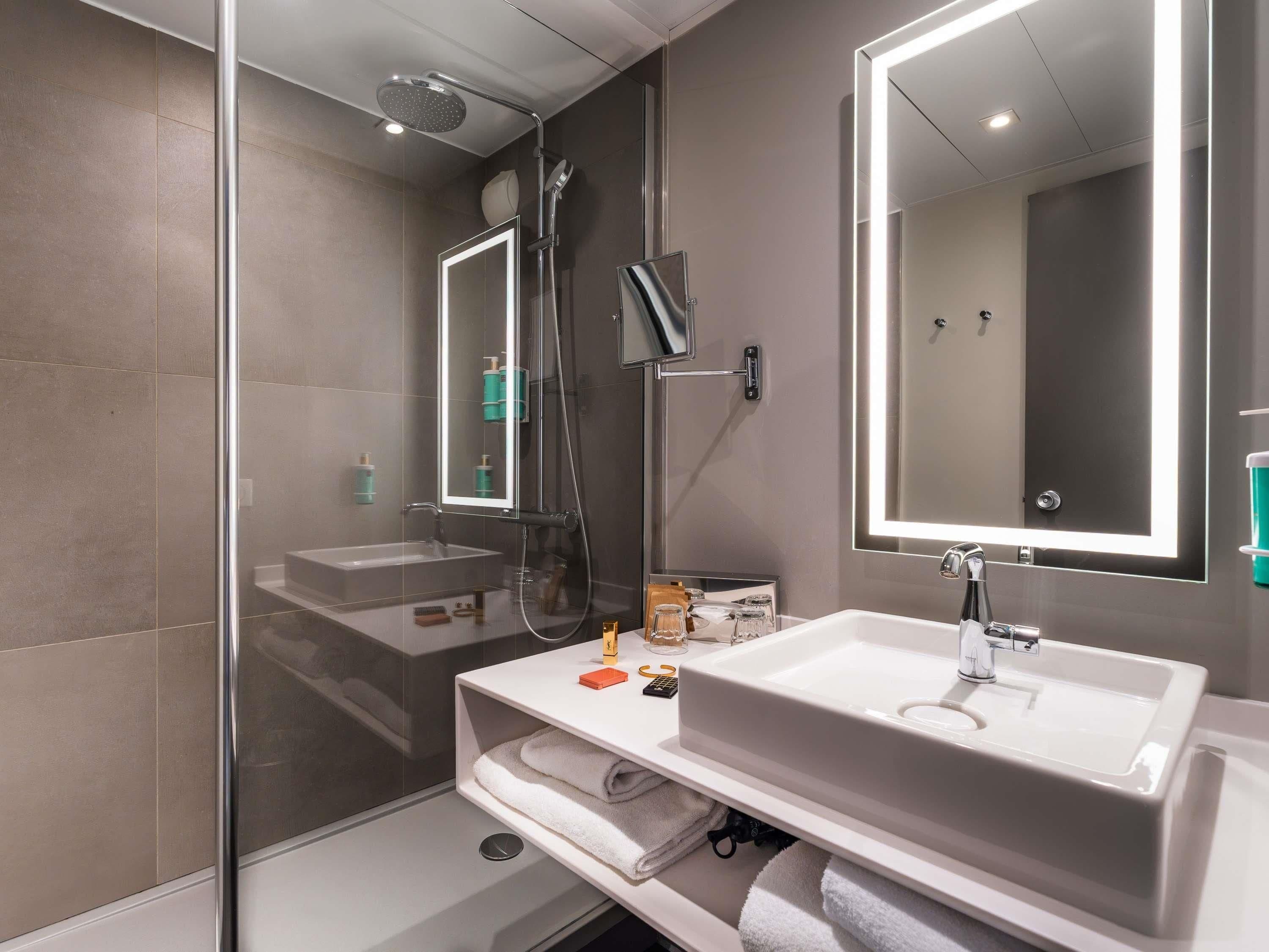 A modern bathroom with a glass-enclosed shower, a large mirror, and a white sink.