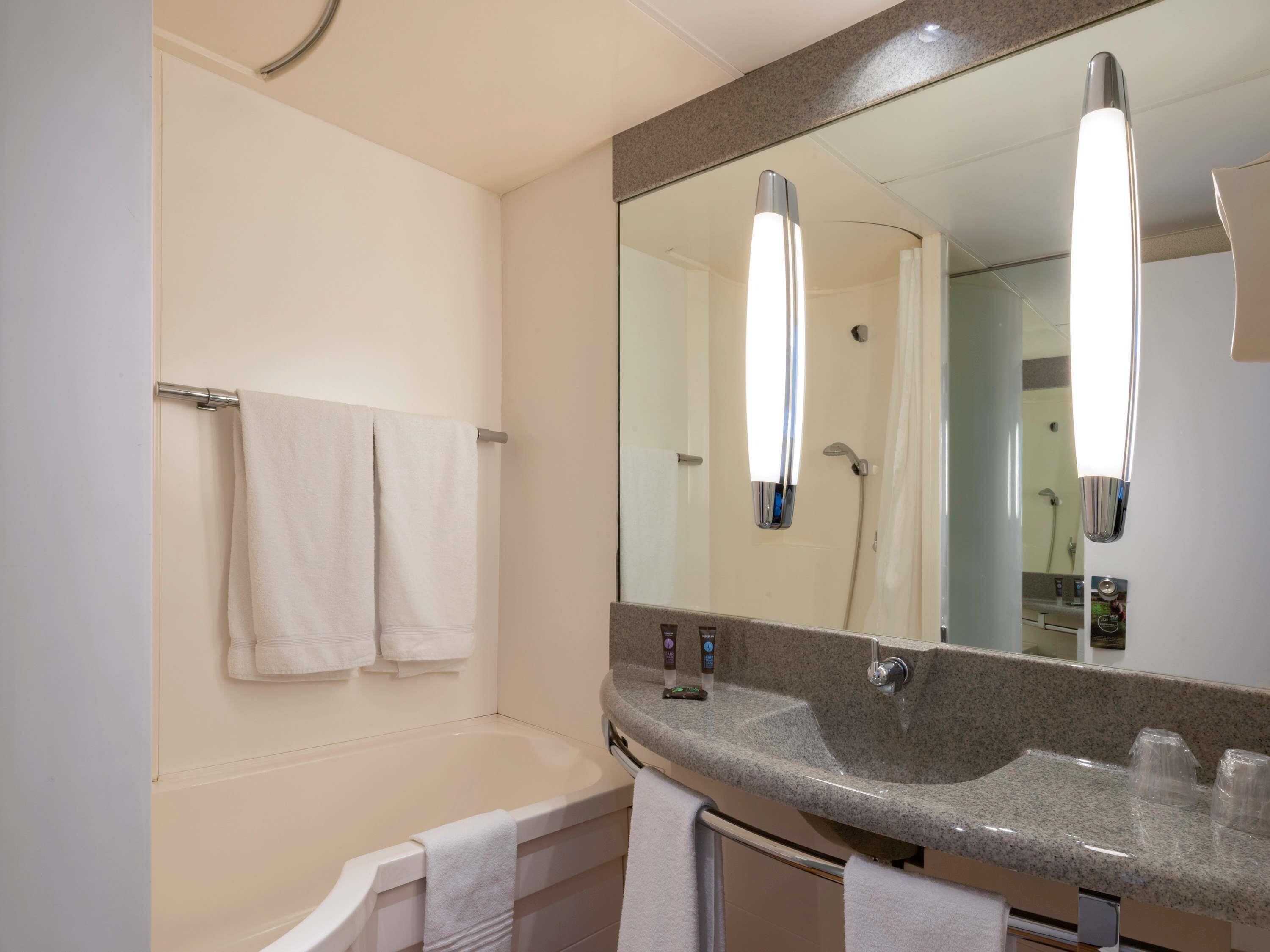 A modern bathroom with a bathtub, a large mirror, and a granite countertop with toiletries.