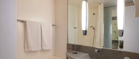 A modern bathroom with a bathtub, a large mirror, and a granite countertop with toiletries.
