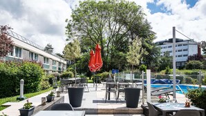 Un patio al aire libre con mesas y sillas, una piscina y un árbol grande.