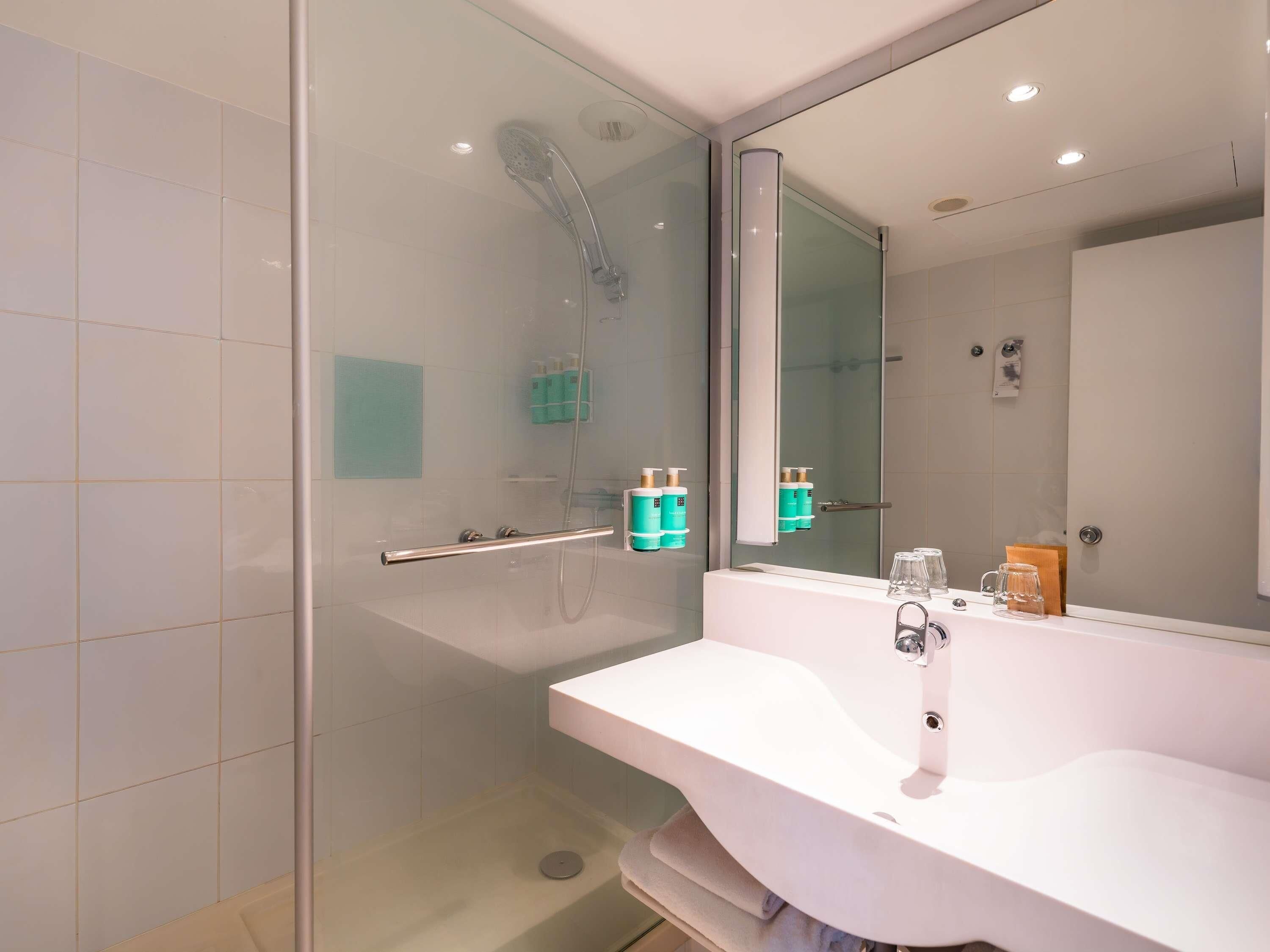 A modern bathroom with a glass-enclosed shower, a white sink, and a large mirror.
