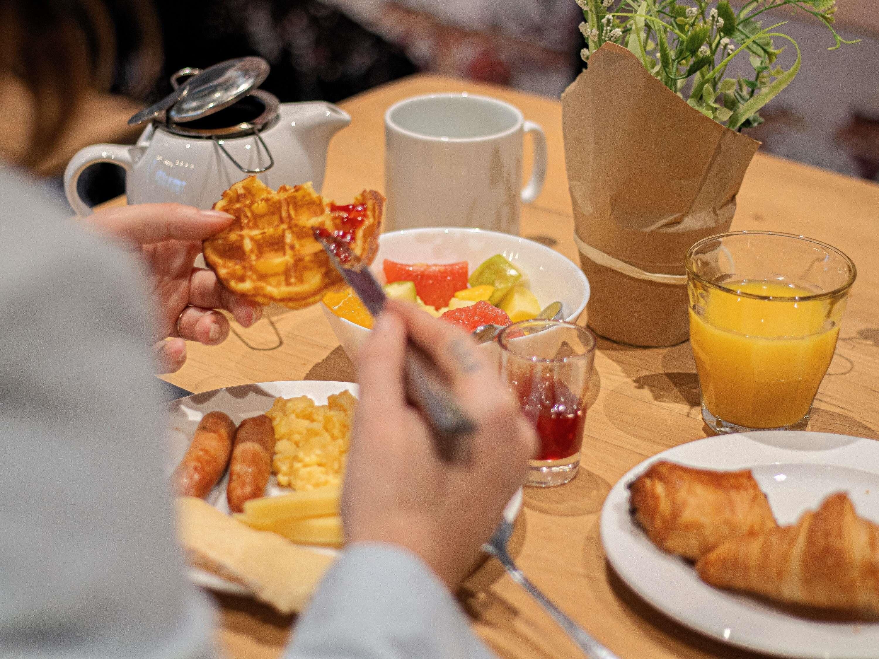A breakfast setting with waffles, fruit, croissants, and juice.