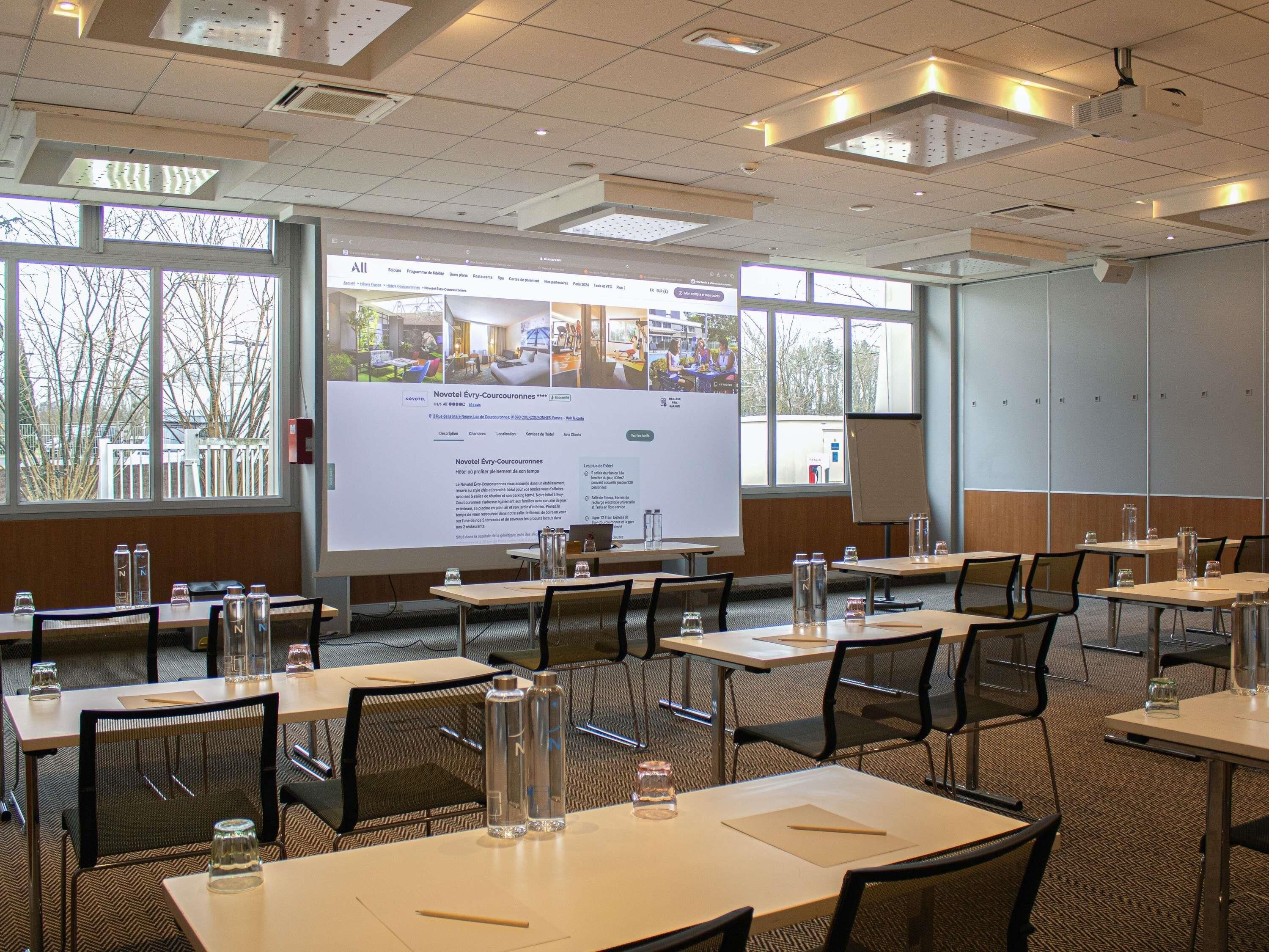 Ein Konferenzraum mit Tischen, Stühlen, einer Projektionsleinwand und Blick auf Bäume.