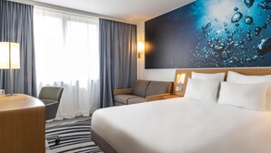 Habitación de hotel con cama, escritorio, silla, sofá y un cuadro grande en la pared.