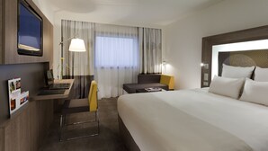 Una habitación de hotel con cama, escritorio, silla y televisor en la pared.