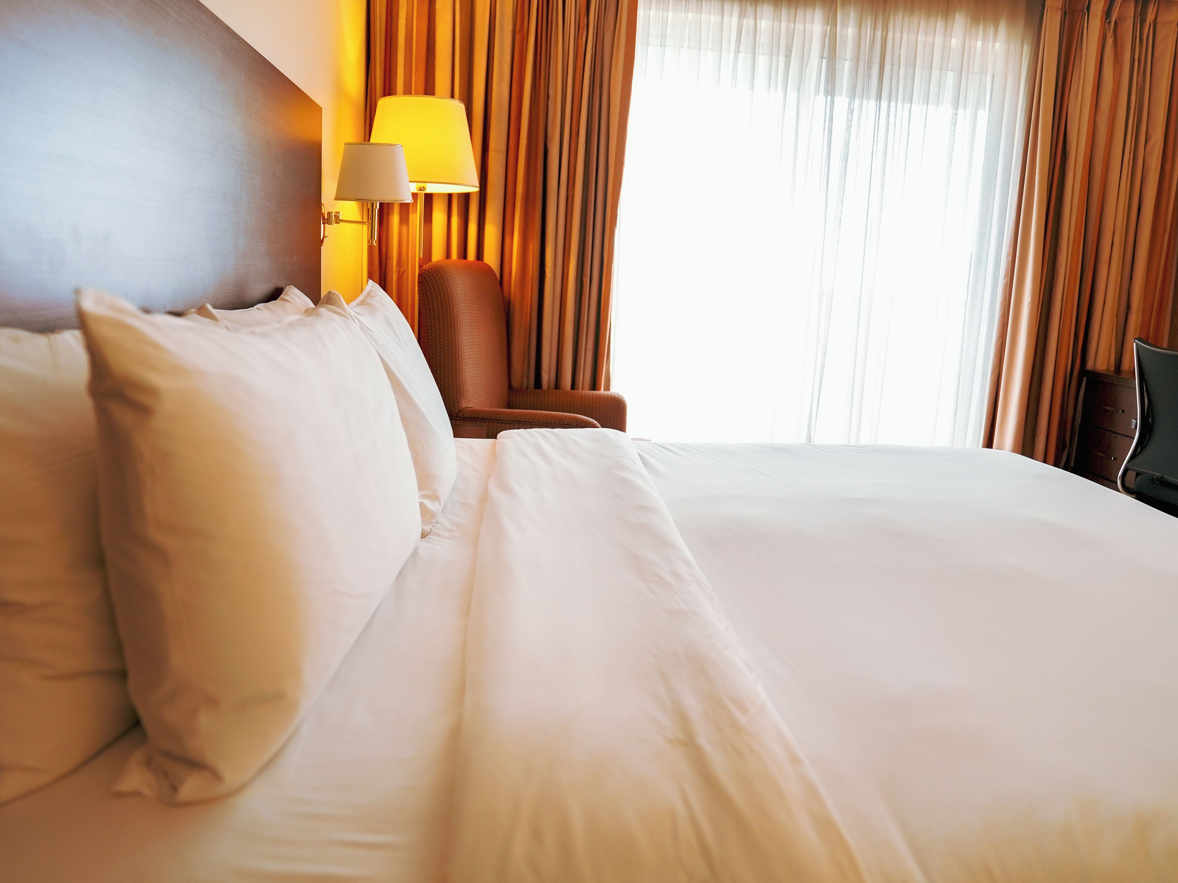 A hotel room with a large bed, a chair, a lamp, and curtains.