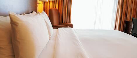 A hotel room with a large bed, a chair, a lamp, and curtains.