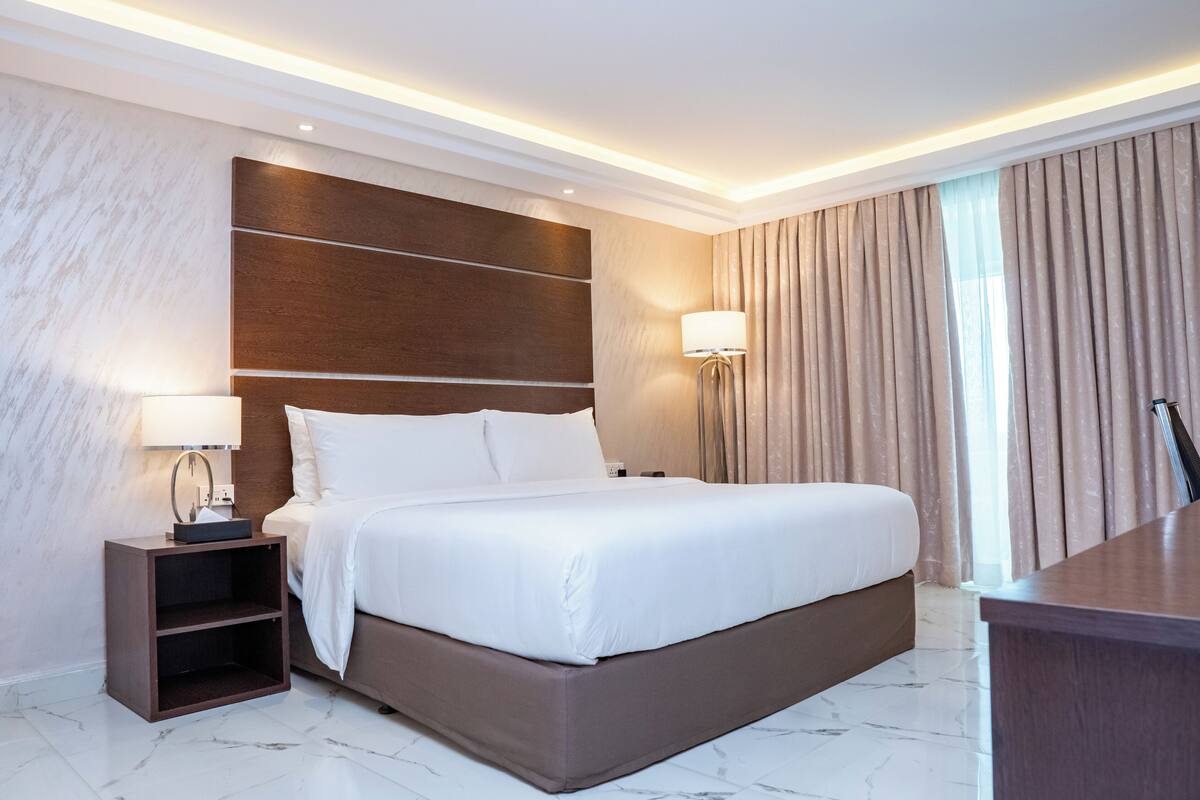 A modern hotel room with a large bed, a nightstand with a lamp, and a desk.