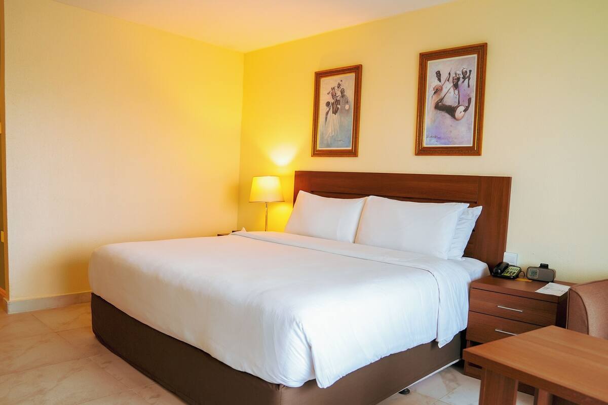 A hotel room with a large bed, a bedside table with a lamp, a phone, and a wooden chair.