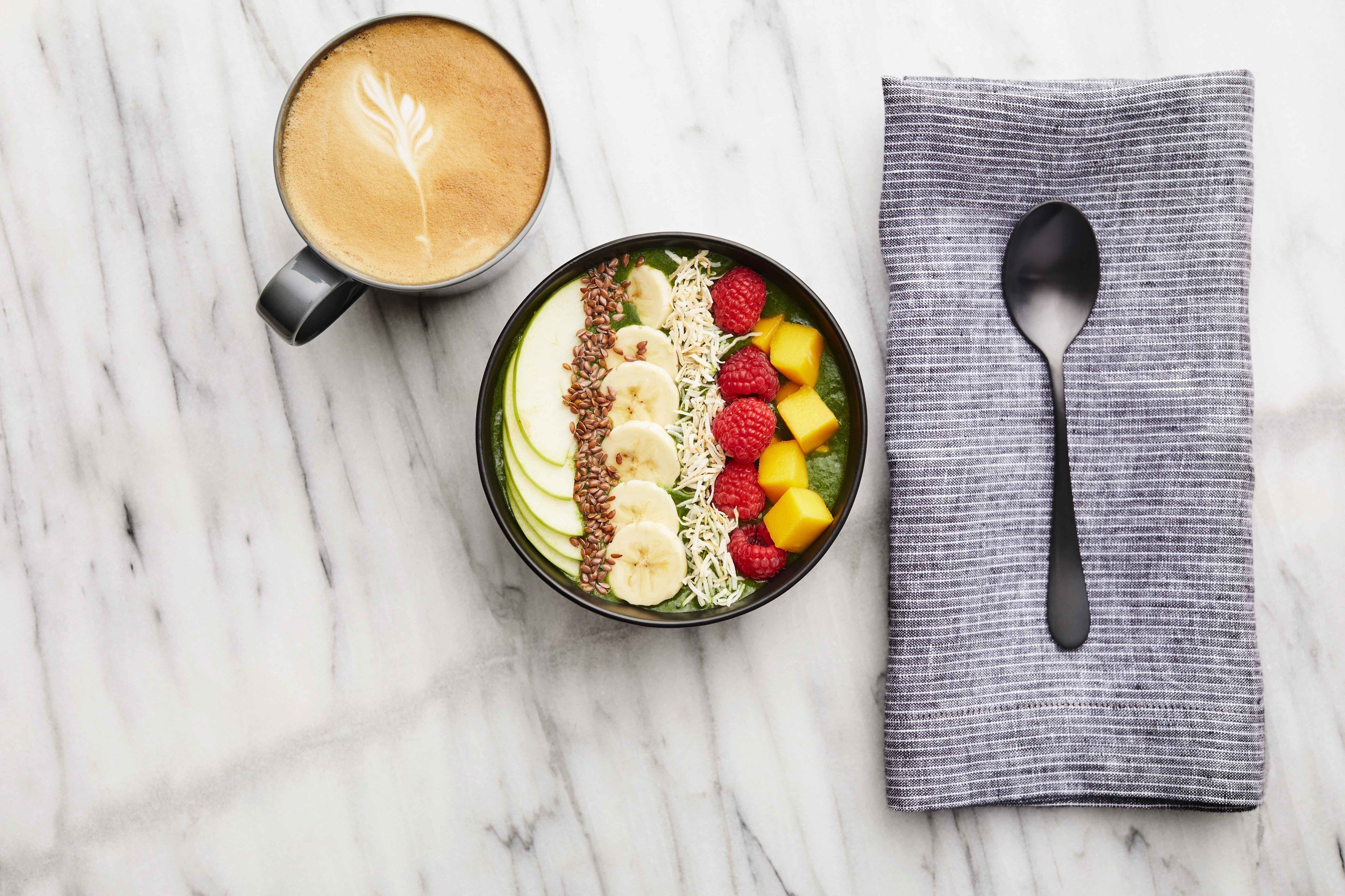 A breakfast setting with a cup of coffee and a bowl of fruit and granola on a marble surface.