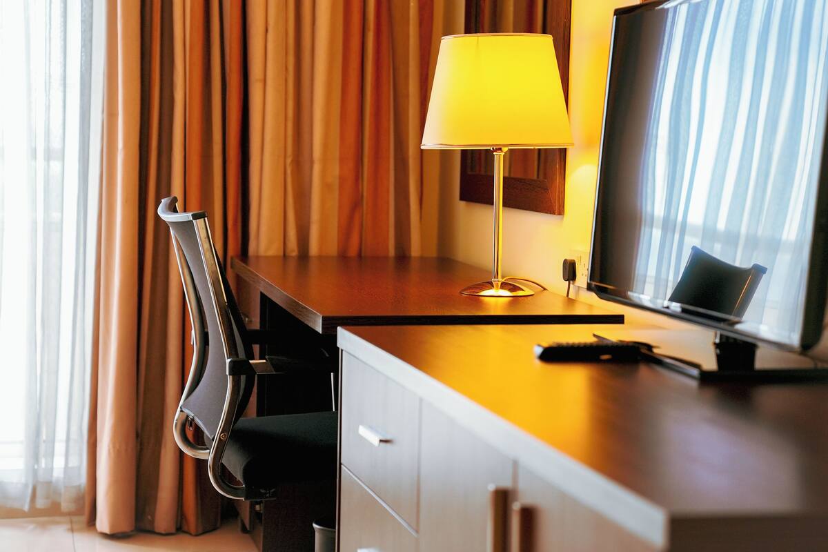 A hotel room with a desk, chair, TV, and curtains.