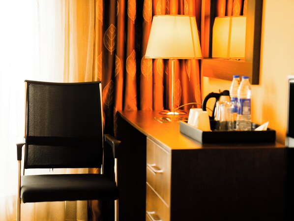 Une chambre d’hôtel avec une chaise noire, un bureau avec une lampe, un miroir et un plateau contenant des articles de toilette.